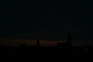 Blick auf eine Stadt im Halbdunkel bei Nacht, schwach beleuchtete Gebäude und Straßen, Symbolbild für Lichtregulierung und Versorgungsunsicherheit