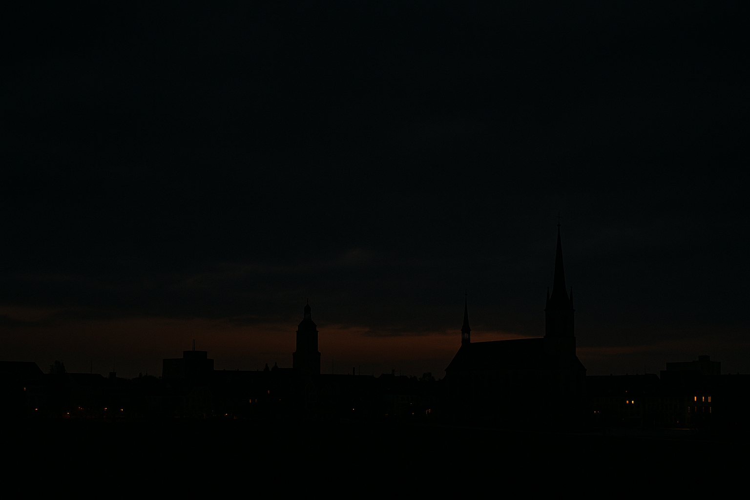 Blick auf eine Stadt im Halbdunkel bei Nacht, schwach beleuchtete Gebäude und Straßen, Symbolbild für Lichtregulierung und Versorgungsunsicherheit